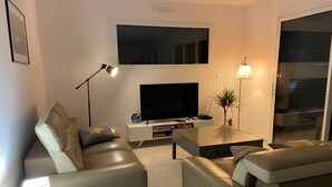 Moderni olohuone, jossa on sohva, sohvapöytä, televisio ja lamppu.