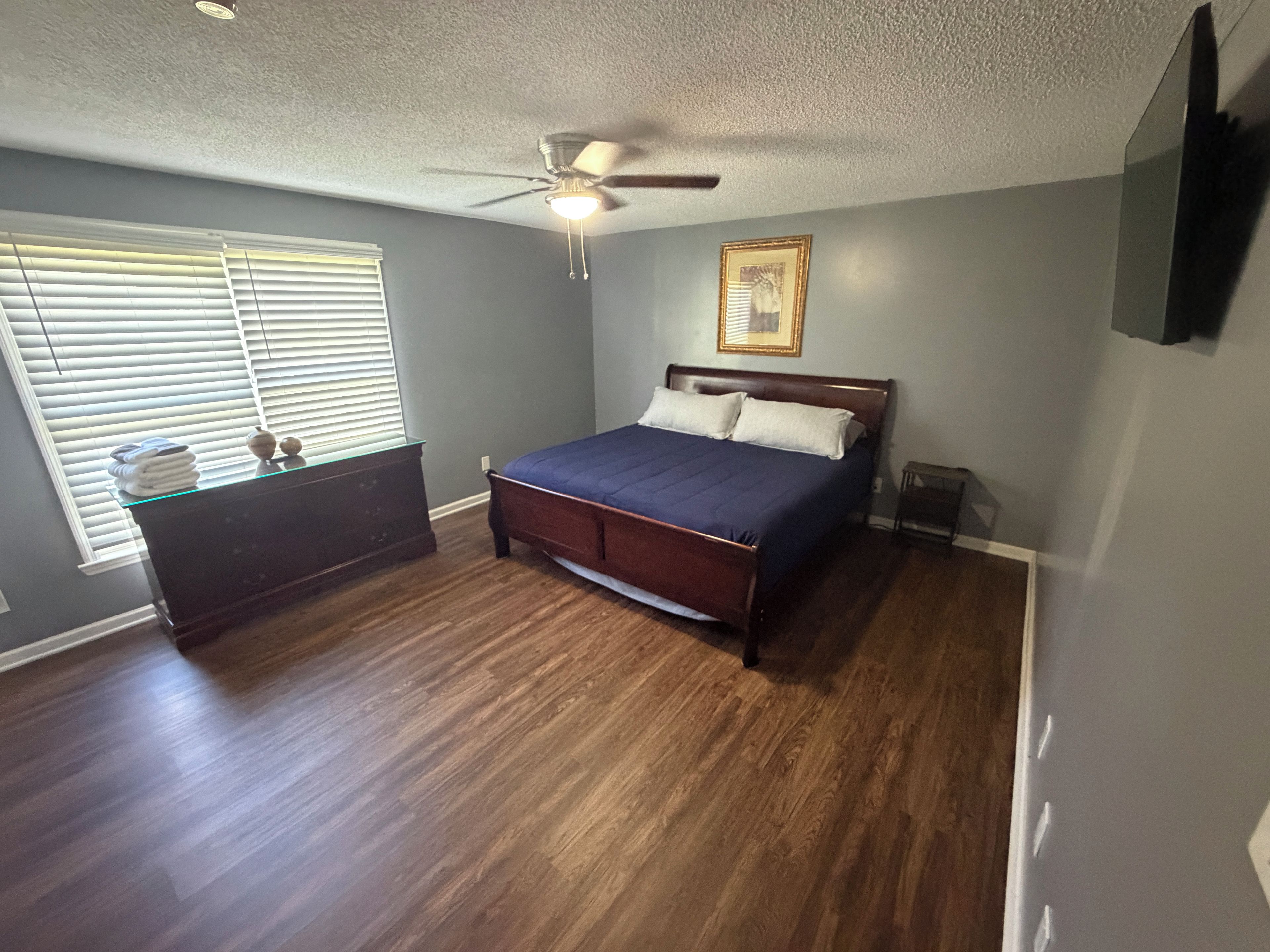 A bedroom with a bed, a ceiling fan, a dresser, and a window with blinds.