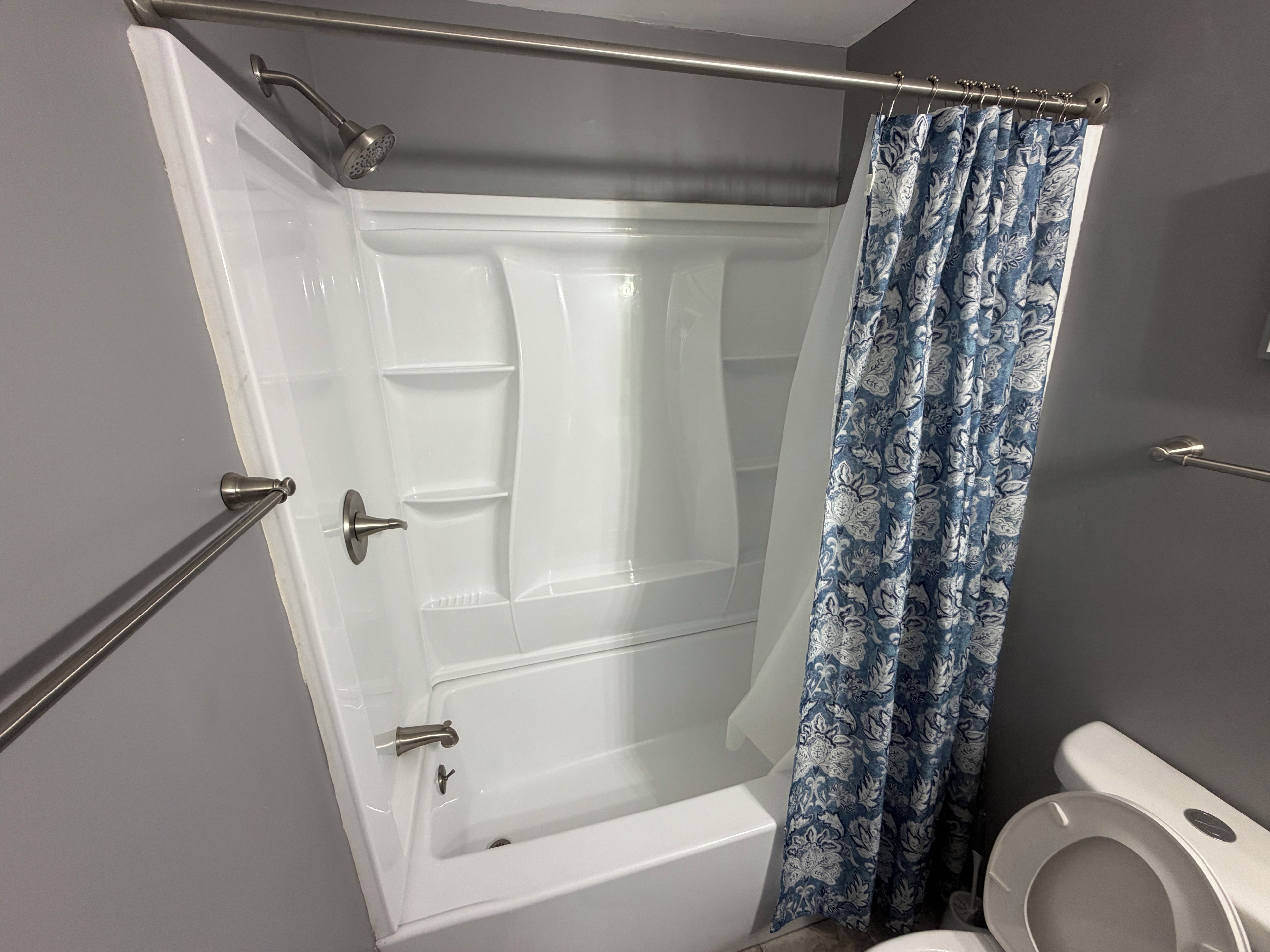 A bathroom with a glass-enclosed shower, a toilet, and a shower curtain with a floral pattern.