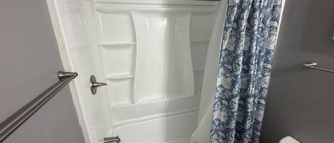 A bathroom with a glass-enclosed shower, a toilet, and a shower curtain with a floral pattern.