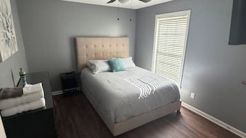 Une chambre à coucher avec un lit, un ventilateur de plafond, une fenêtre avec des stores et une porte.