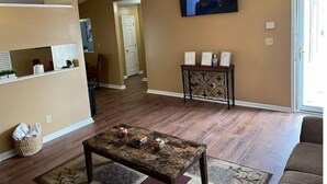 A living room with a ceiling fan, a television mounted on the wall, a coffee table, and a door leading to another room. - Beautiful Private 3 Bedroom Home (Albany)