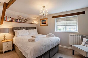 Un dormitorio con cama, mesita de noche, lámpara, estanterías, candelabro, ventana y radiador.