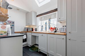Una cocina moderna con armarios blancos, encimera de madera, horno empotrado y una ventana con persianas decorativas.
