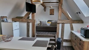 Cocina compacta con comedor, vigas de madera, televisor de pantalla plana y escalera que lleva a un dormitorio tipo altillo.