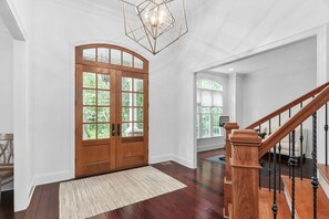 Ein geräumiger Eingangsbereich mit einer Holztür, einem großen Fenster und einer Treppe mit schwarzer Geländer.