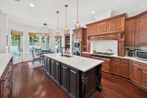 Een ruime keuken met een groot eiland, houten kastjes en moderne apparatuur.