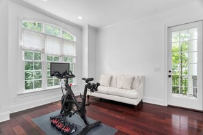 Ein Zimmer mit einem stationären Fahrrad, einer Yogamatte und einem weißen Sofa.