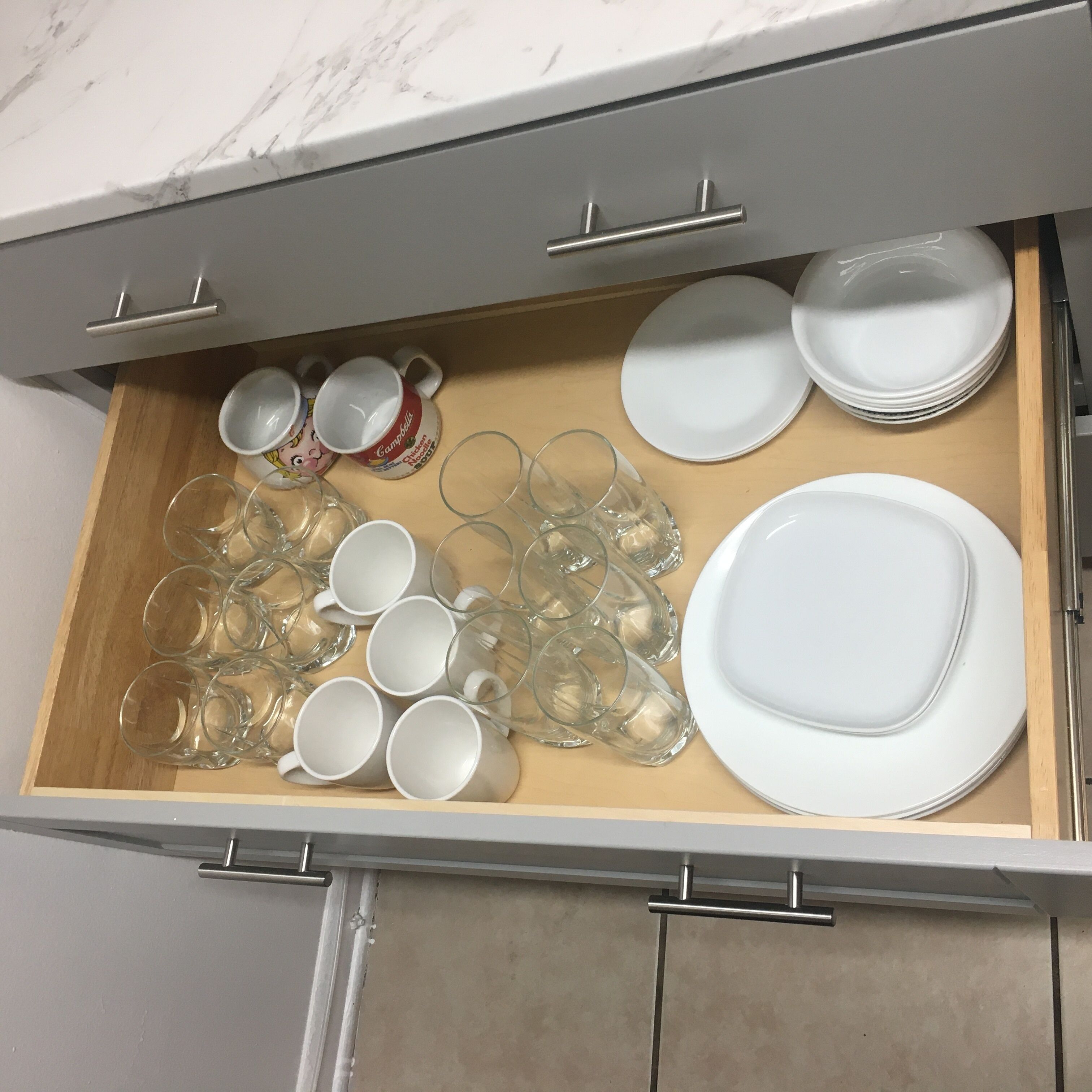 A drawer containing white plates, clear drinking glasses, and a few mugs.