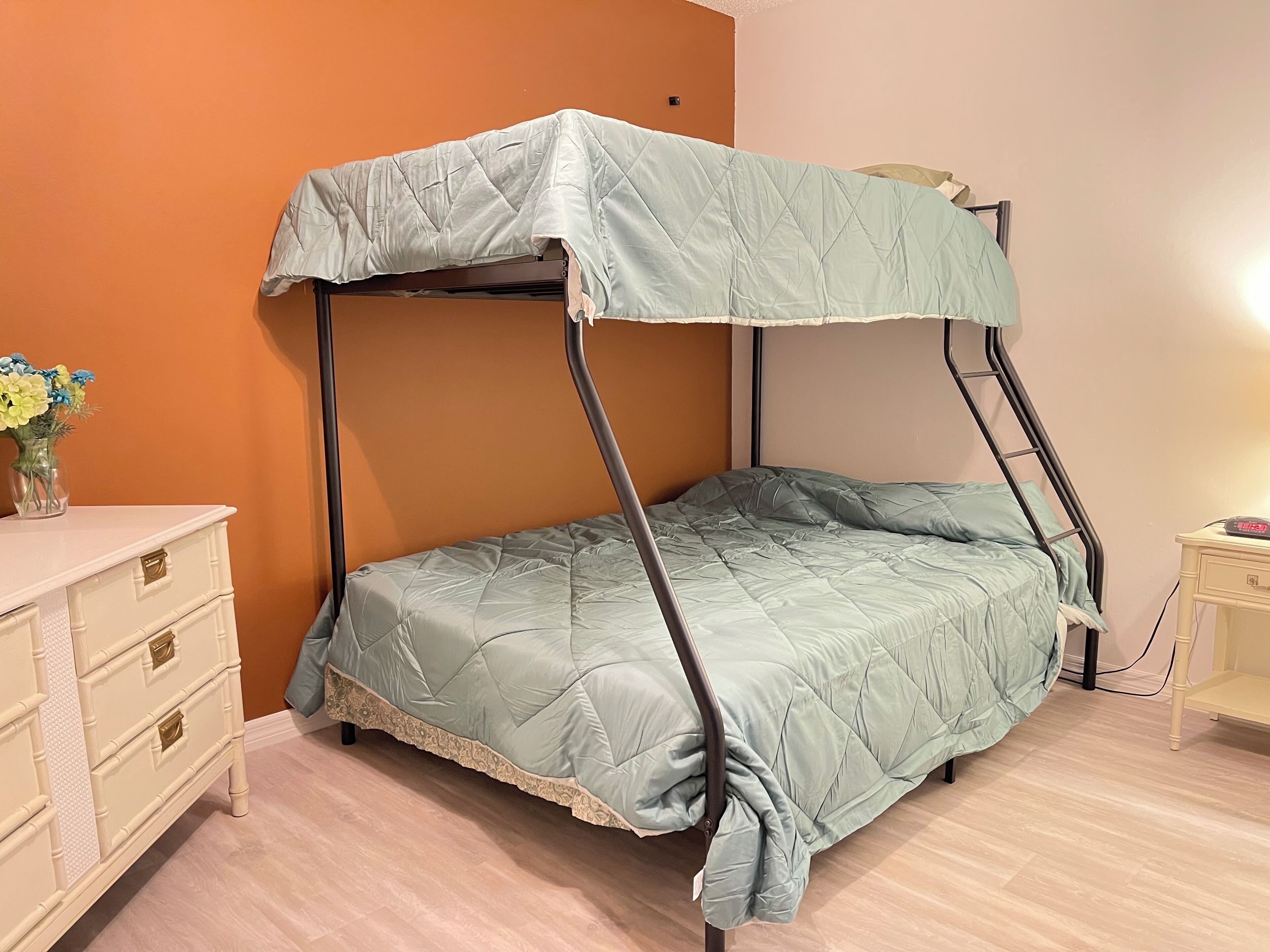 Un lit simple avec un baldaquin, une table de chevet avec une lampe et une commode avec des tiroirs.