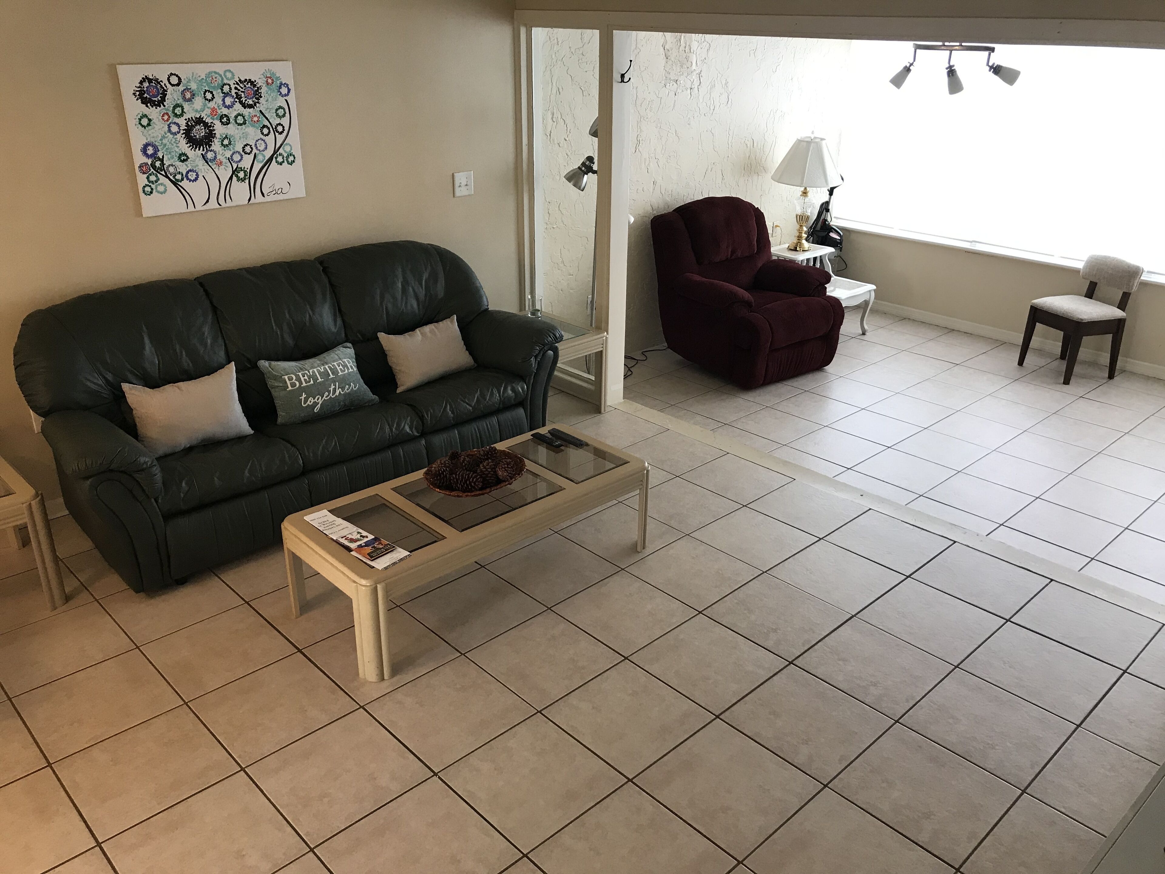A living room with a dark green leather sofa, a white coffee table, and a red armchair. There is a painting on the wall and a lamp on a side table.