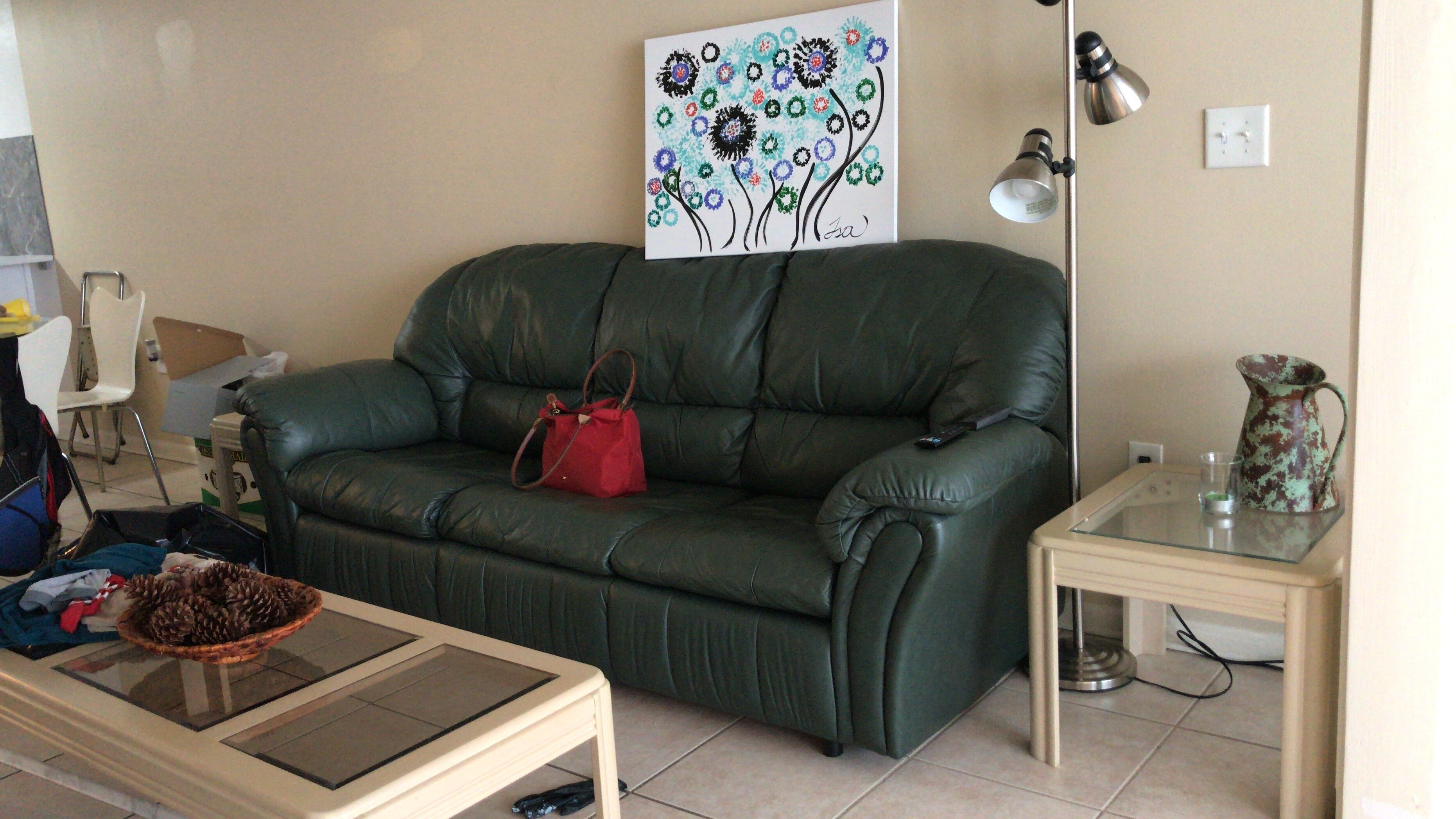 A living room with a green leather sofa, a small table with a basket, a lamp, and a painting on the wall.