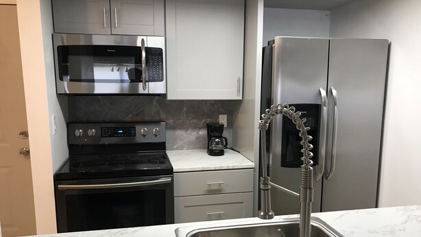 A compact kitchen with a stainless steel refrigerator, a microwave, a stove, and a sink with a modern faucet. - Historic Section of Sebring  Townhome (Sebring)