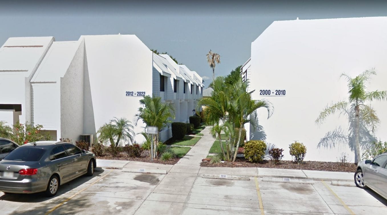 Un parking rempli de voitures et un chemin menant à un bâtiment divisé en deux sections, dont les panneaux indicateurs affichent les dates « 2012-2022 » et « 2000-2010 ».