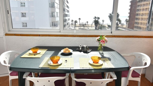 Uma mesa de jantar com vista para um hotel e palmeiras pela janela.