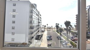 Um edifício de vários andares com uma placa 'CENTER', um estacionamento cheio de carros e vista para palmeiras e uma praia.