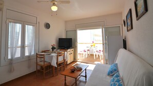 Uma sala de estar com sofá, televisão, mesa de jantar com cadeiras e varanda com mesa e cadeiras.