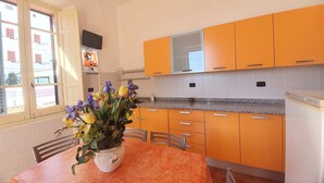Keittiössä on oranssit kaapit, graniittitaso ja ruokapöytä, jonka päällä on maljakko täynnä kukkia.
