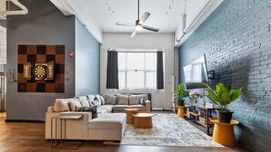 A modern living room with a sectional sofa, a ceiling fan, a large window with curtains, a dartboard, and a potted plant. - *New* Huge!  Spacious 3 Bedroom in Oakland that sleeps 12! over 3000+ sq ft (Pittsburgh)