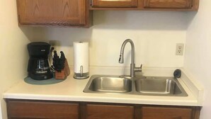 Una cocina con armarios de madera, un lavamanos de acero inoxidable, una cafetera y un rollo de toallas de papel.