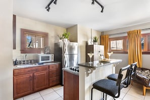 A compact kitchen with wooden cabinets, a stainless steel refrigerator, a microwave, and a small island with seating.