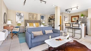 En moderne stue med sofa, sofabord og et lille køkkenområde med et køleskab og barstole.