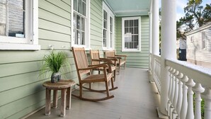 A porch with rocking chairs and a small table with a plant. - Great Neighborhood Restaurants | Lewis Court - A (Charleston)