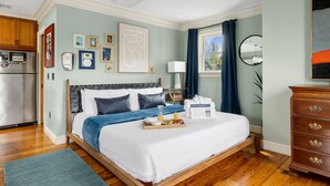 Une chambre d’hôtel comprenant un lit, un plateau de petit-déjeuner, une commode en bois et un coin cuisine avec un réfrigérateur.