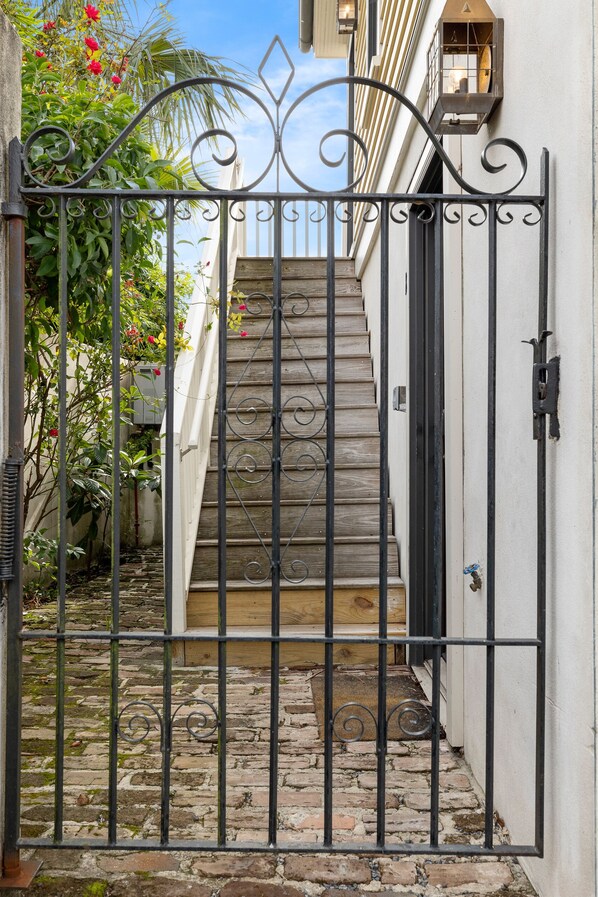 Une entrée fermée par un portail, avec un escalier en bois menant à un bâtiment.