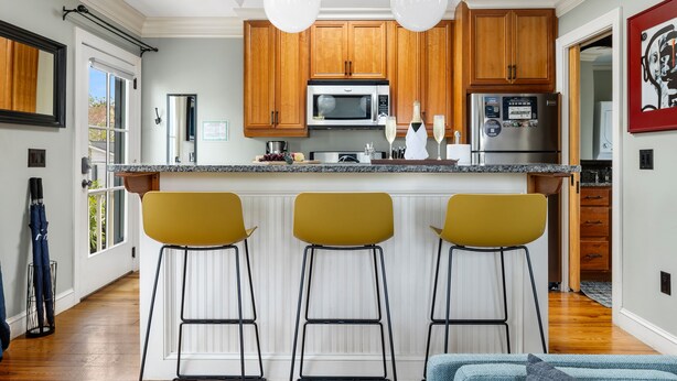 Une cuisine moderne avec des meubles en bois, un îlot central doté de tabourets de bar et une grande fenêtre.