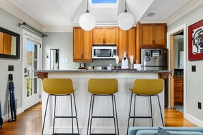 Une cuisine moderne avec des meubles en bois, un îlot central doté de tabourets de bar et une grande fenêtre.