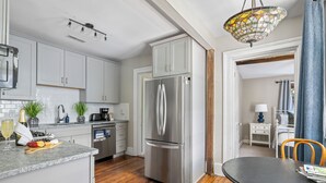 A modern kitchen with white cabinets, a stainless steel refrigerator, a wooden dining table, and a chandelier.