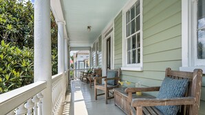 A porch with wooden chairs and a table, a railing, and a view of the street.