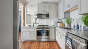 A modern kitchen with stainless steel appliances, white cabinetry, and a wooden floor.