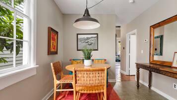 A dining area with a round table, wicker chairs, a potted plant, and a hanging light fixture.