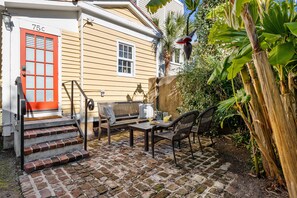 A house with a red door labeled "75C," a brick staircase, outdoor furniture, and a garden with banana plants.