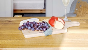 Ein Zimmer mit einem Bett, einer rosafarbenen Wand, einem Spiegel und einem Tisch mit Käse, Trauben und einem Glas Champagner.