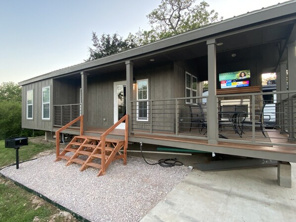 Una casa moderna con un porche cubierto, mobiliario exterior y una televisión.