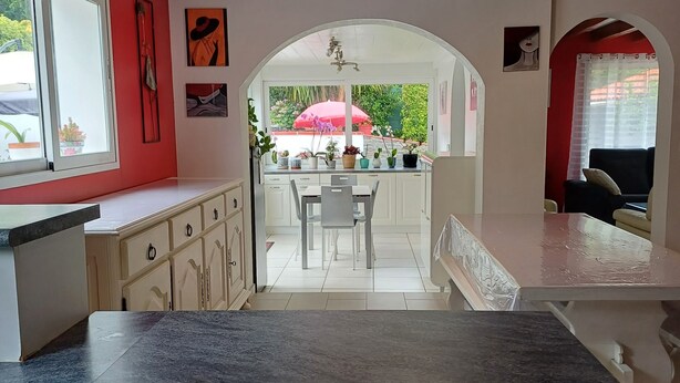 A kitchen with a granite countertop, white cabinets, and a view through an archway to a dining area with a table and chairs. - Charming Basque house with jacuzzi, close to the ocean (Saint-Jean-de-Luz)