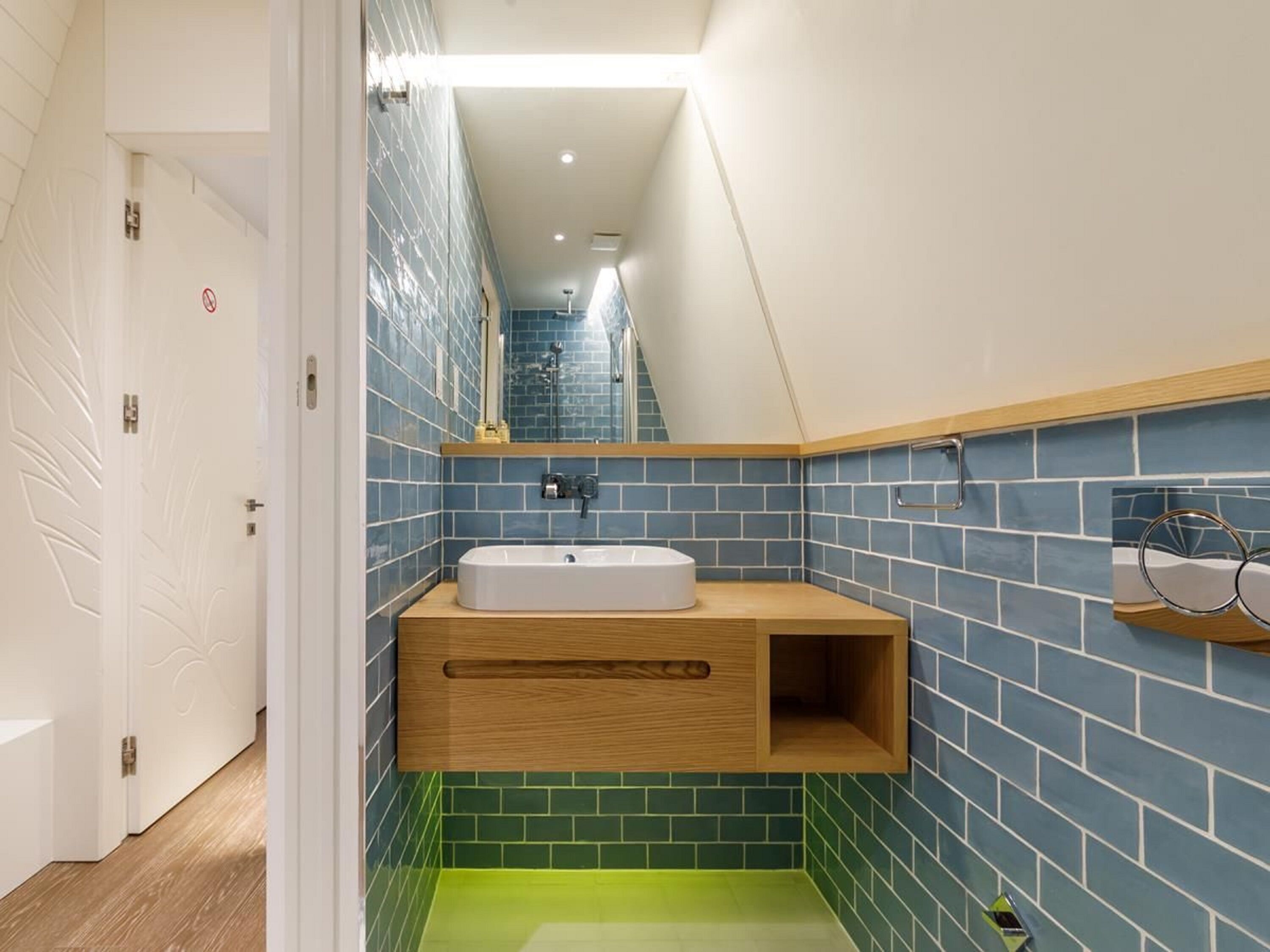 Une salle de bain avec un lavabo blanc, un meuble-lavabo en bois et des murs recouverts de carreaux bleus et verts.