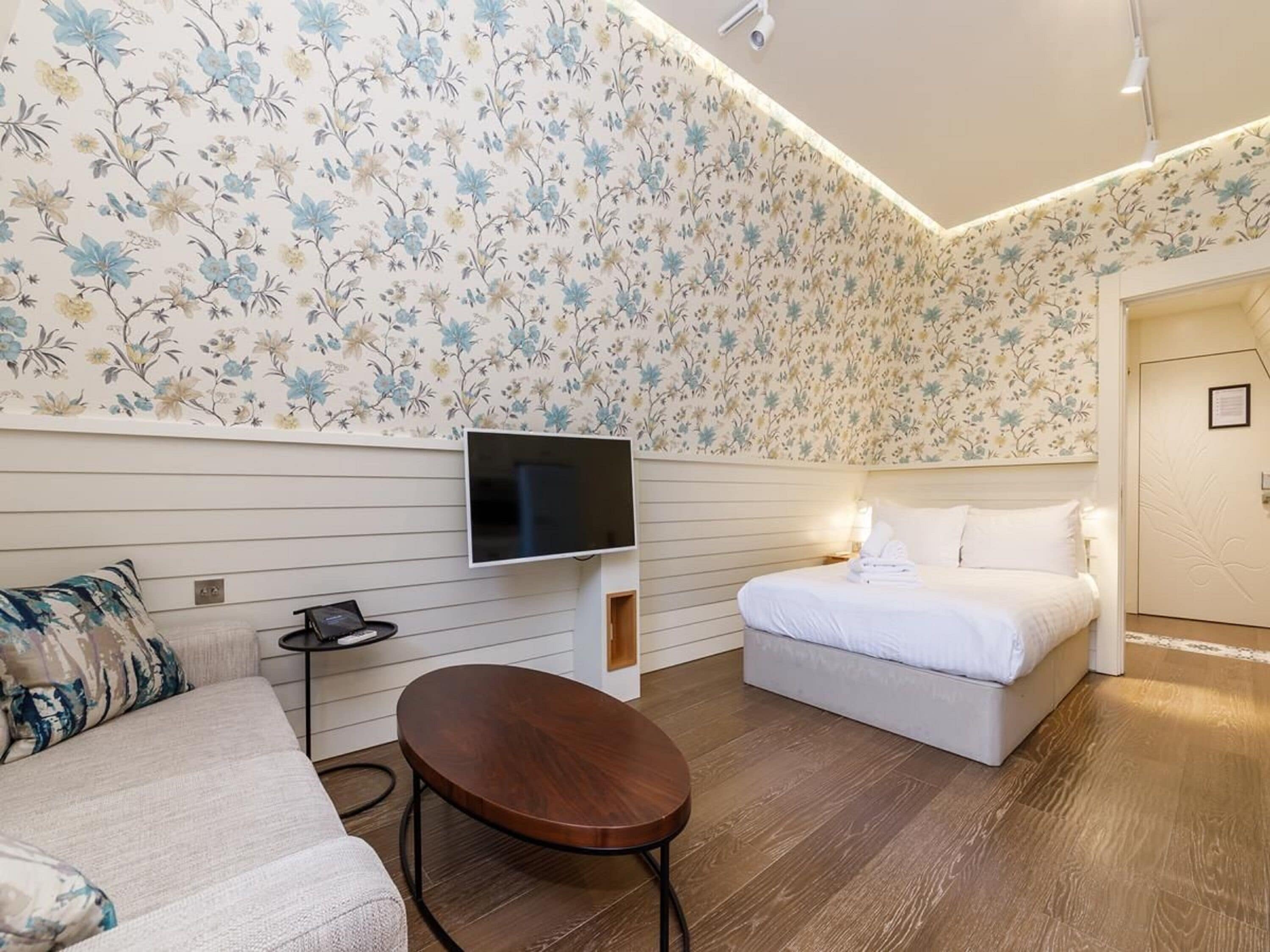 Een moderne hotelkamer met bloemenbehang, een flatscreen-televisie, een bed, een bank en een klein houten tafeltje.