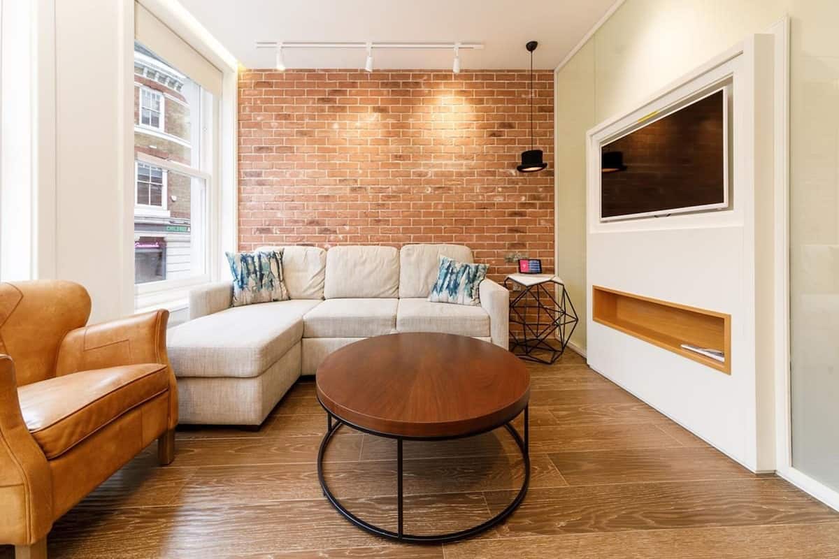 A modern living room with a sectional sofa, a round coffee table, and a brick wall.