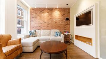 A modern living room with a sectional sofa, a round coffee table, and a brick wall.