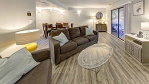 A modern living room with a brown sofa, glass coffee table, and a dining area with wooden chairs and a table. - Short breaks in September and October live now! (Rehoboth Beach)