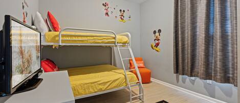 A bunk bed room with a television, Mickey Mouse wall decal, and a window with curtains.