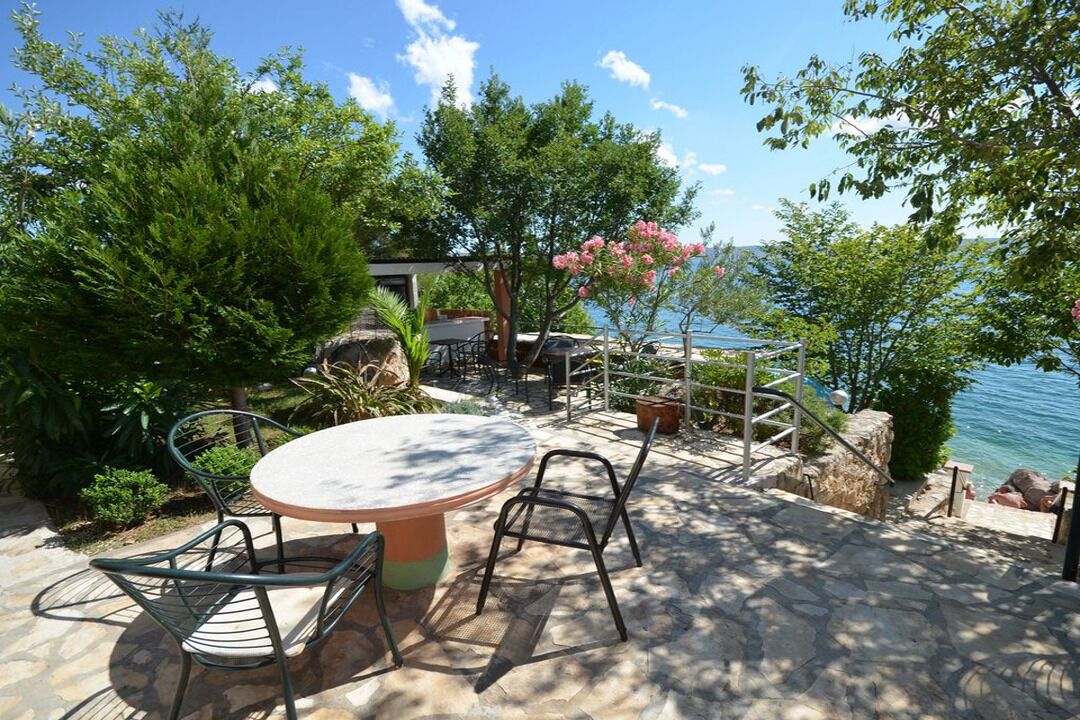 Patio esterno con tavolo rotondo e sedie, immerso nel verde con vista su un corpo d'acqua.