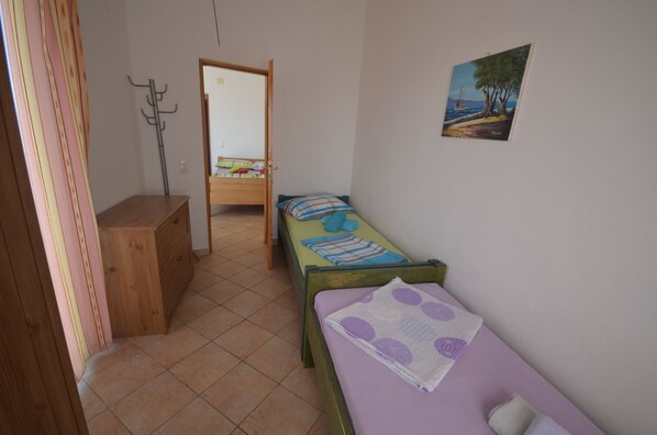 A room with a bed, a wooden dresser, a coat rack, and a painting on the wall.