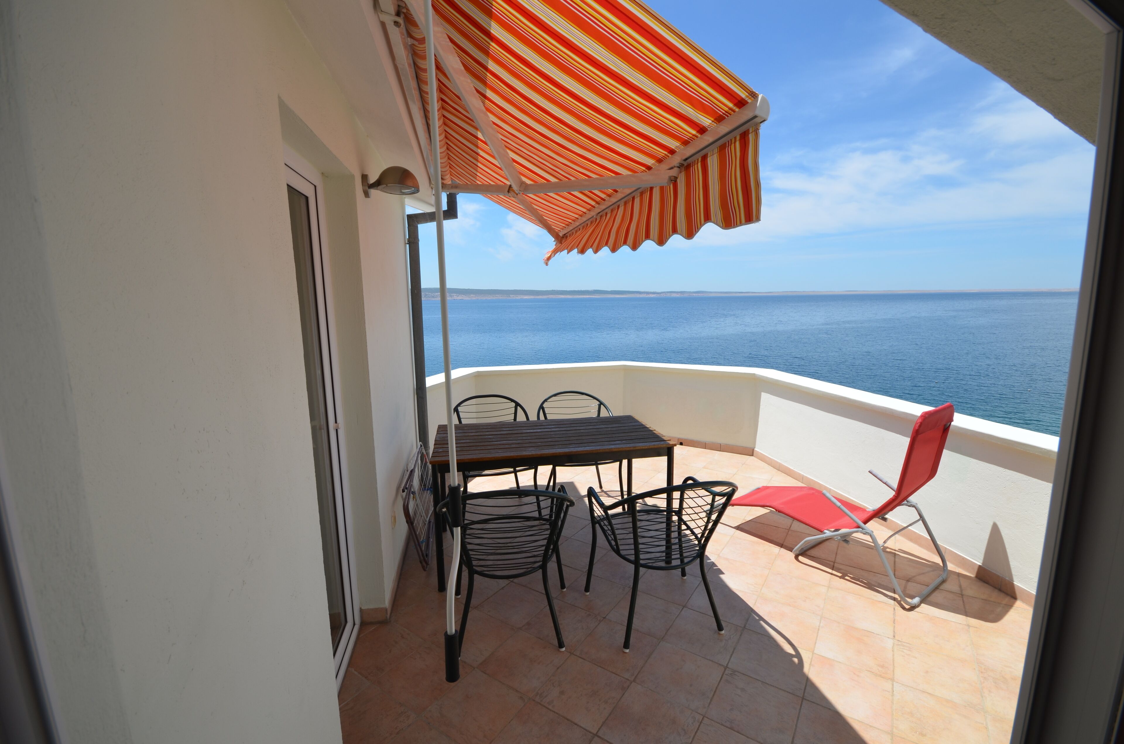A balcony with a table and chairs, a striped awning, and a view of the sea.