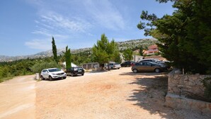 A gravel parking area with several cars parked, surrounded by trees and a stone wall. - 2-raum-apartment/studio , Adria Paradies - Direkt am Meer+privat (Starigrad Paklenica)