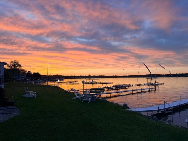 Une vue sur le lac, avec des bateaux amarrés, une zone herbeuse et un coucher de soleil.